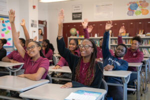 Picture of high school students in classroom raising their hands. 