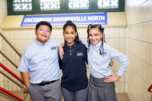 1 male and 2 female students smiling and hugging shoulders in school stairwell