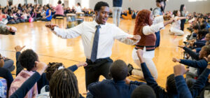 Teacher and students taking part in joyful community-building activity during community circle in gymnasium