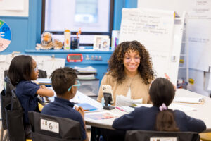female teacher smiling and looking at students sat across her